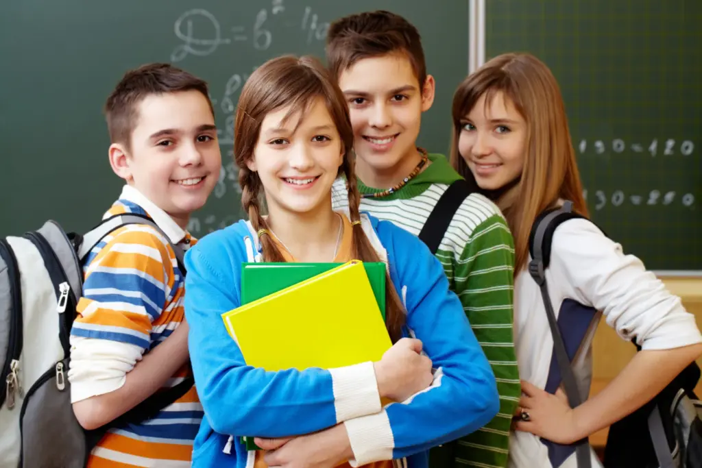 Schülerinnen und Schüler stehen vor einer Tafel und lächeln in die Kamera
